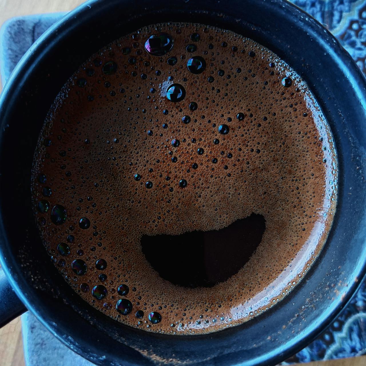 Top view of rich and frothy Turkish coffee in a black mug, creating a smiley face pattern.